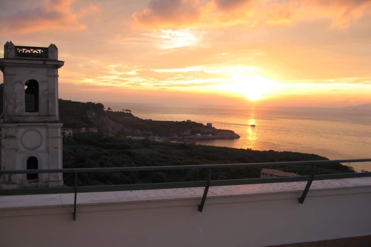 Une vue sur le coucher de soleil en bord de mer, avec un clocher et une balustrade de balcon.