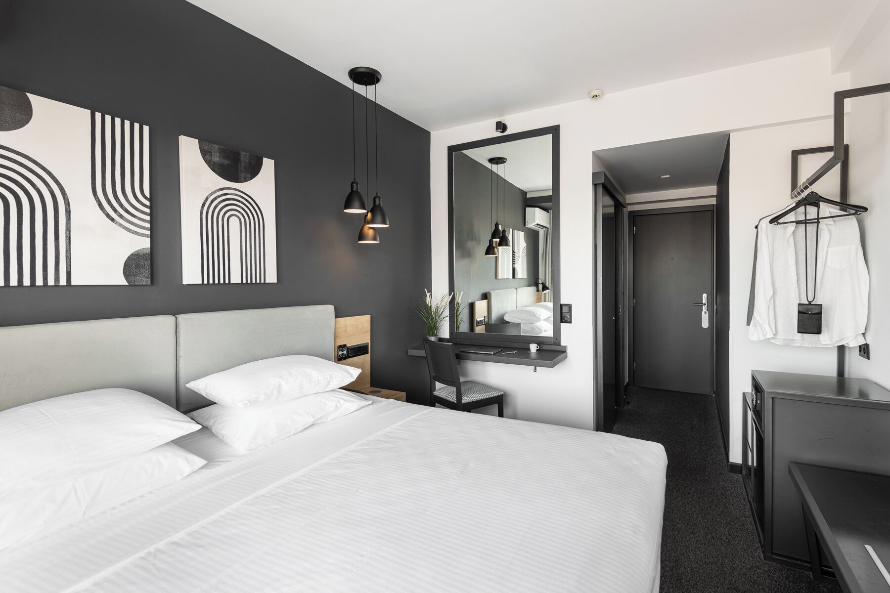 Ein modernes Hotelzimmer mit einem großen Bett, einem Schreibtisch und einem Spiegel.