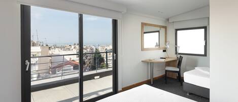 Habitación de hotel con un gran ventanal corredero, un escritorio con silla, una cama y ventana con vistas a la ciudad.
