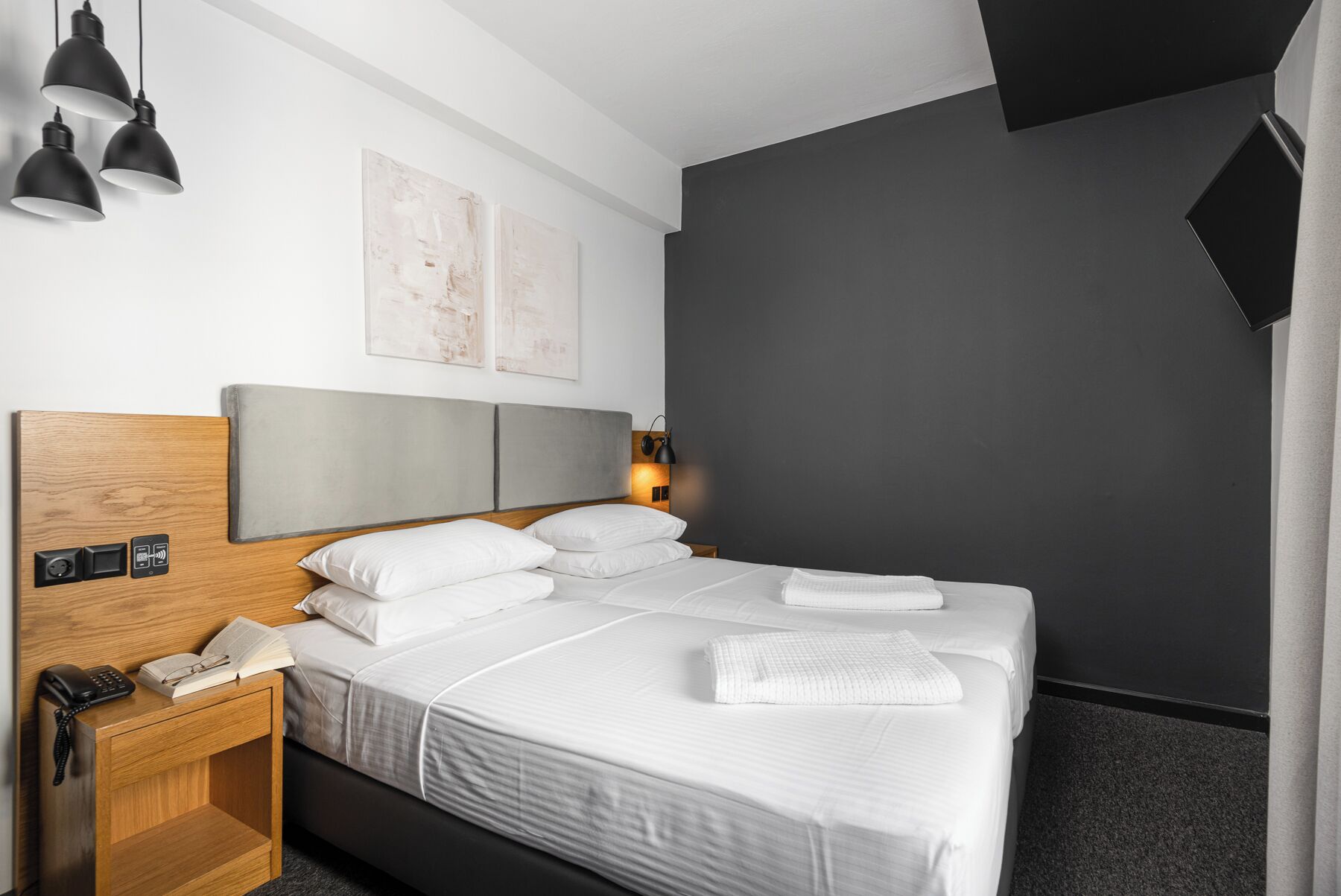 Ein modernes Hotelzimmer mit einem großen Bett, Nachttischen, einem Schreibtisch mit Telefon und Kunstwerken an der Wand.