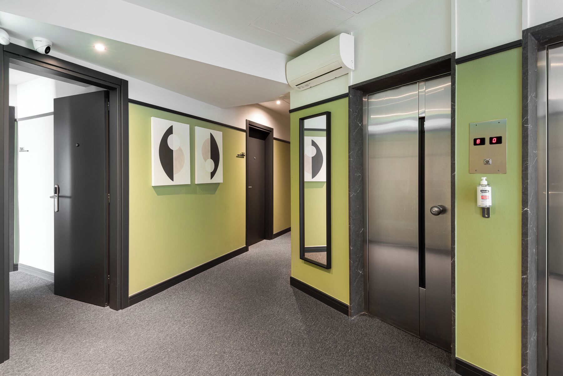 A hallway with green walls, two elevators, and artwork on the walls.