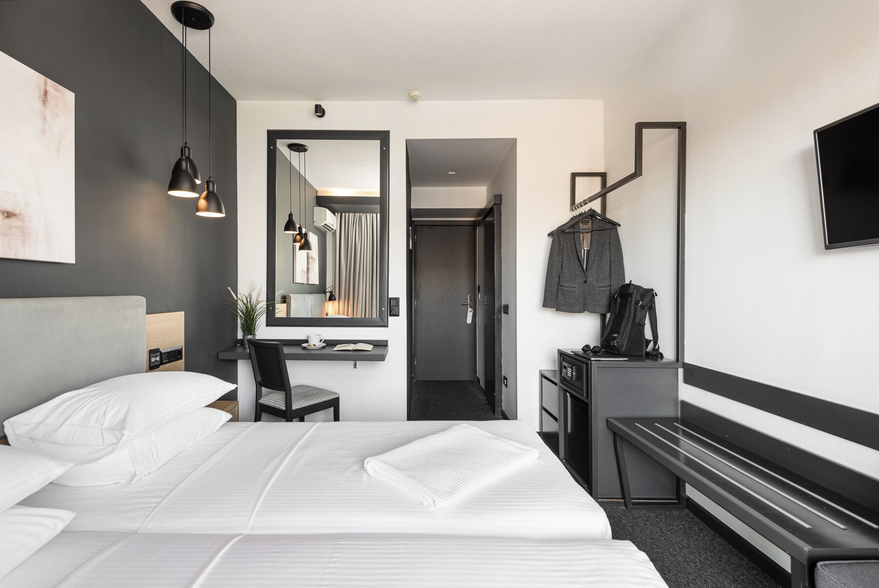 Una habitación de hotel moderna con una cama grande, un escritorio, un espejo, un banco y un televisor.