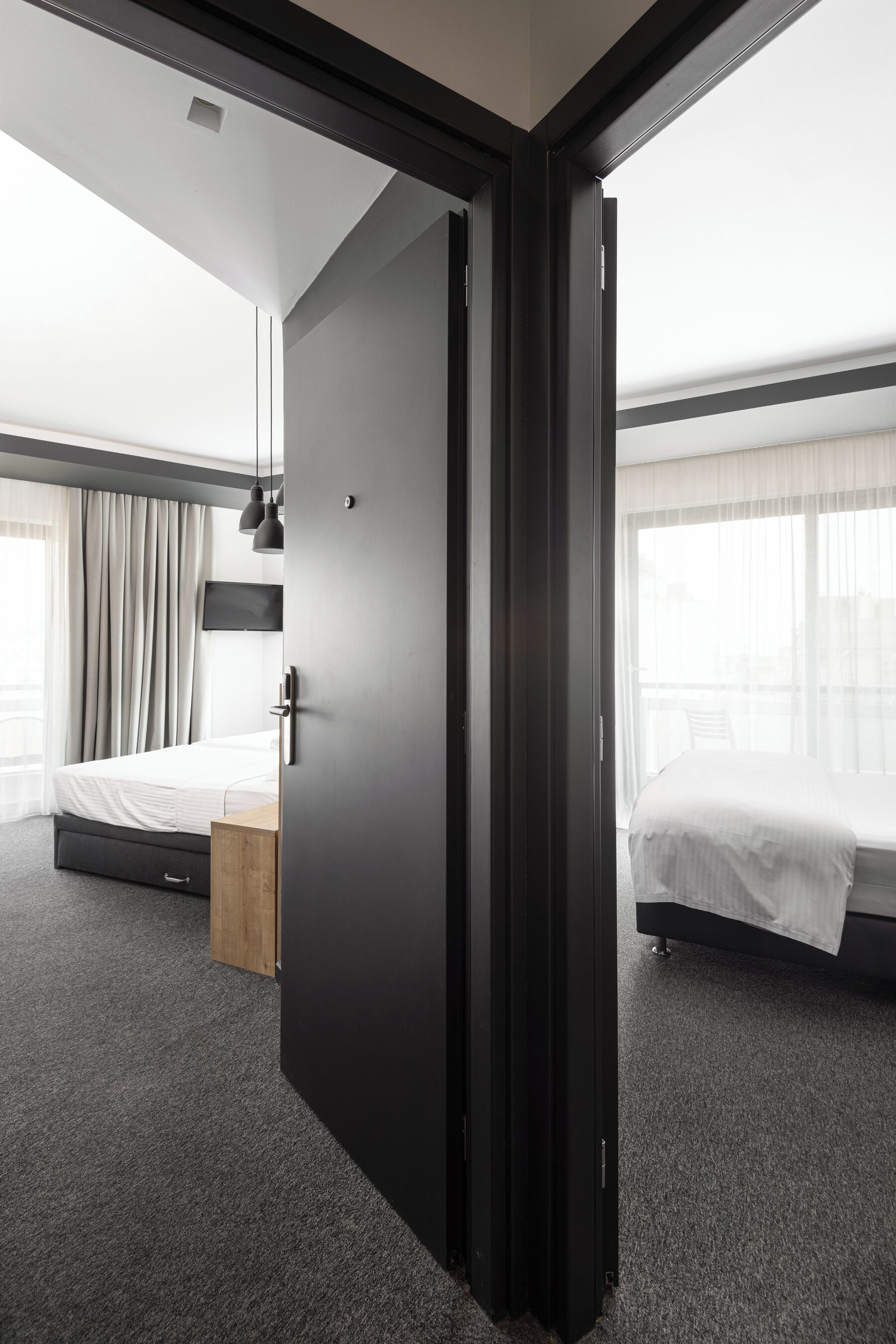 A modern hotel room with a large bed, a wooden nightstand, a desk, and a TV mounted on the wall.