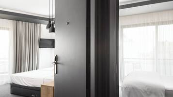 A modern hotel room with a large bed, a wooden nightstand, a desk, and a TV mounted on the wall.