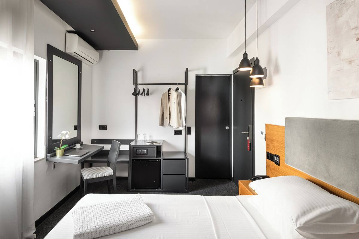 A hotel room with a bed, a desk with a chair, a wardrobe, and a hanging shoe rack.