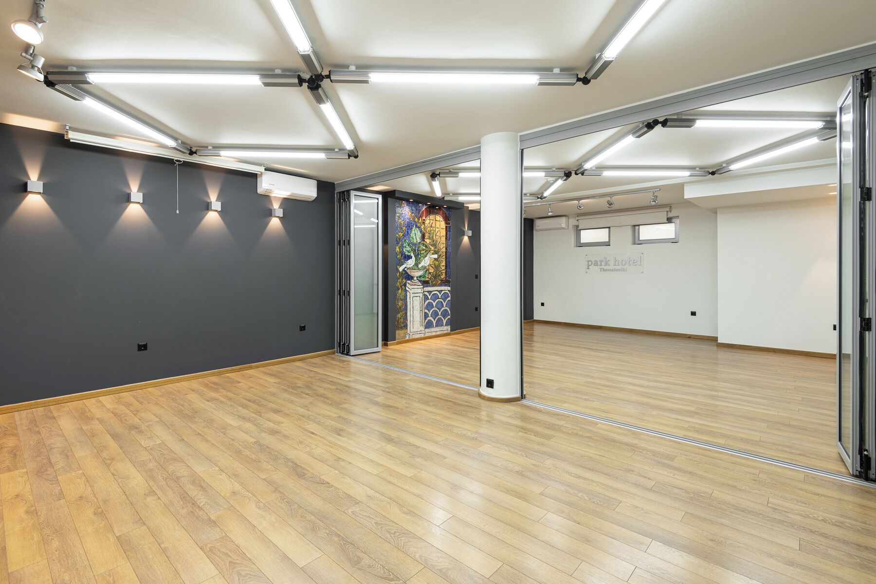 A spacious room with wooden flooring, a large mirror, and a mural on the wall.