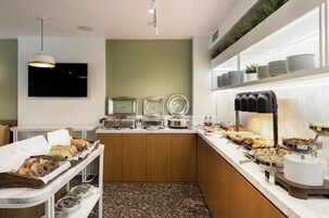 A modern kitchen with buffet-style food service, including bread, pastries, and hot beverages.