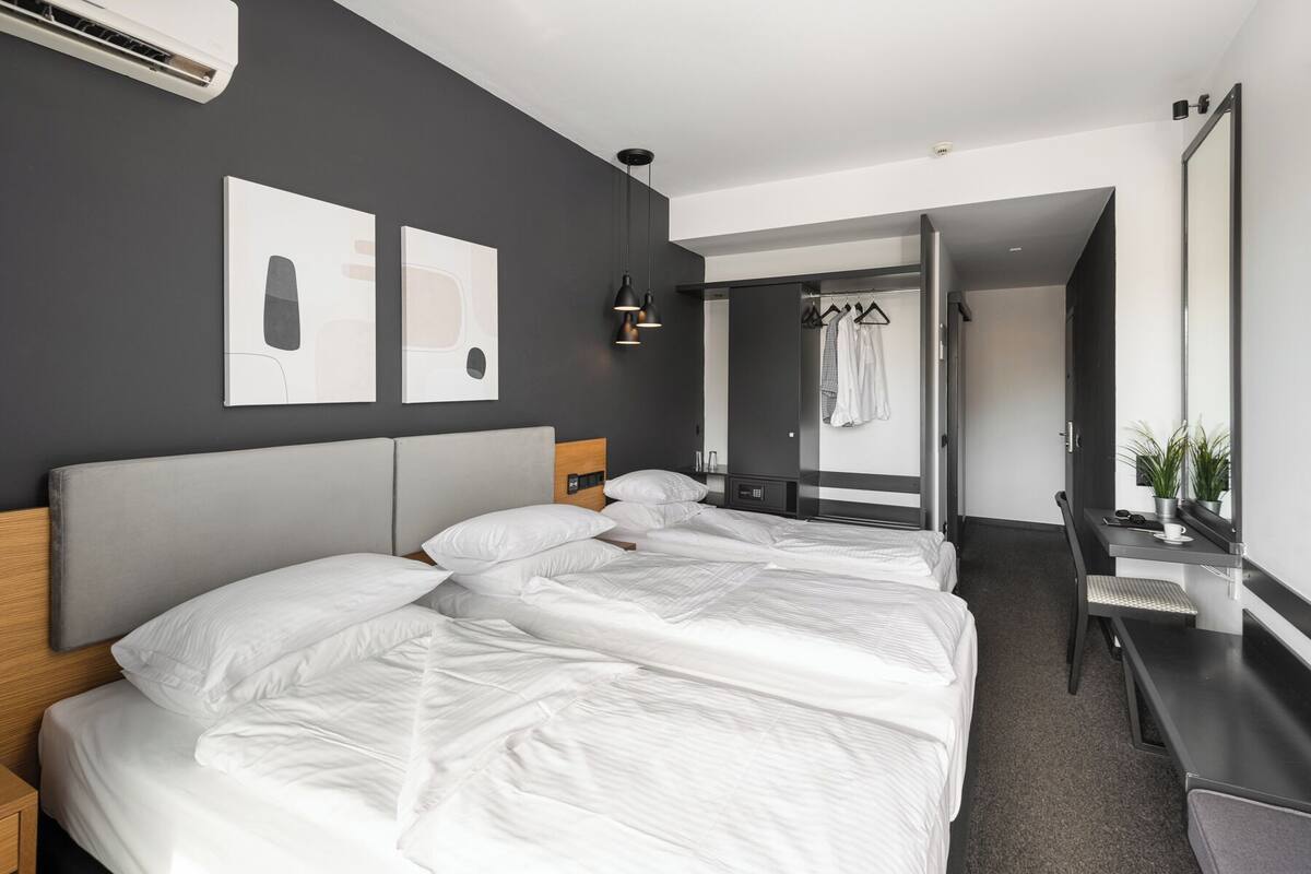 A modern hotel room with a large bed, bedside tables, a desk, and a mirror.