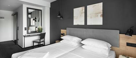 Una habitación de hotel moderna con una cama grande, un escritorio con silla, un espejo y cuadros en la pared.