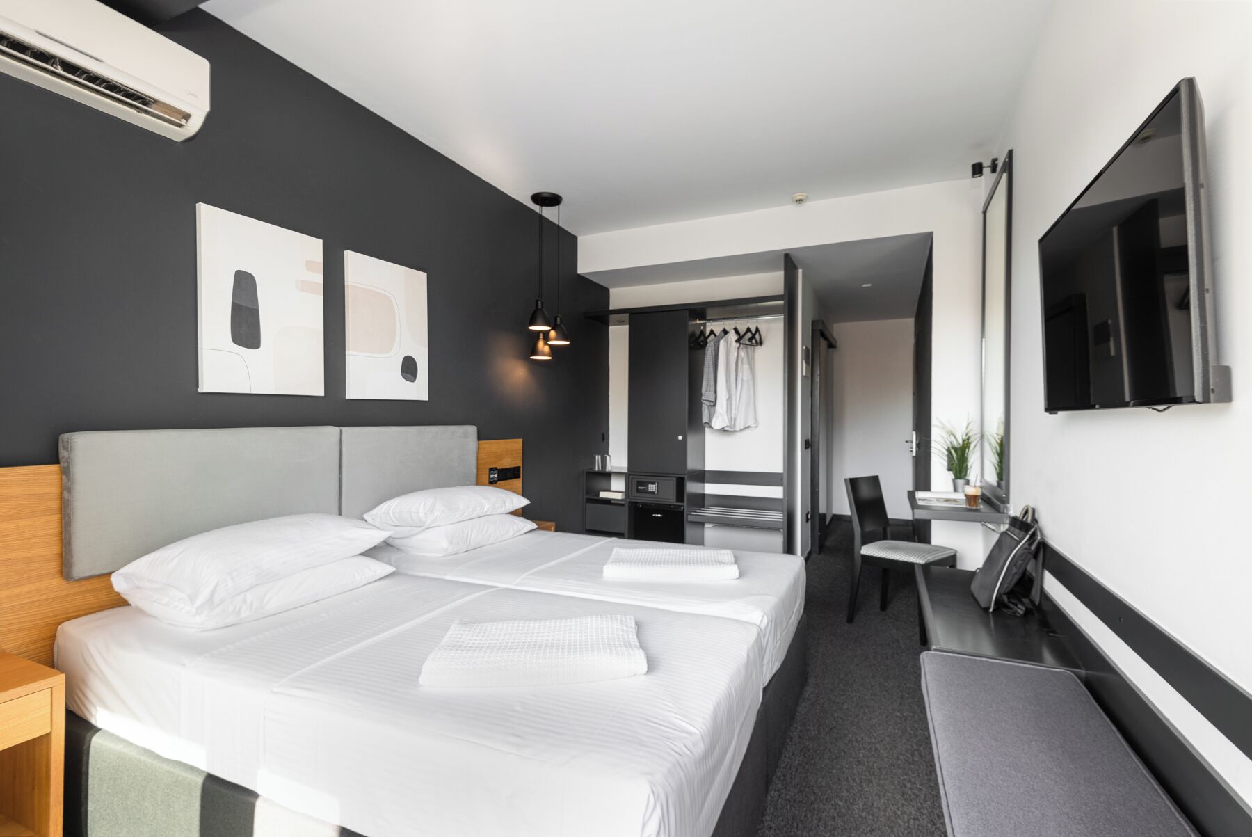 A modern hotel room with a large bed, a desk, a chair, a TV, and artwork on the wall.