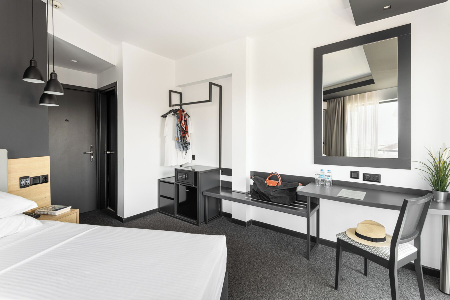 Quarto de hotel com cama, escrivaninha, cadeira e espelho.