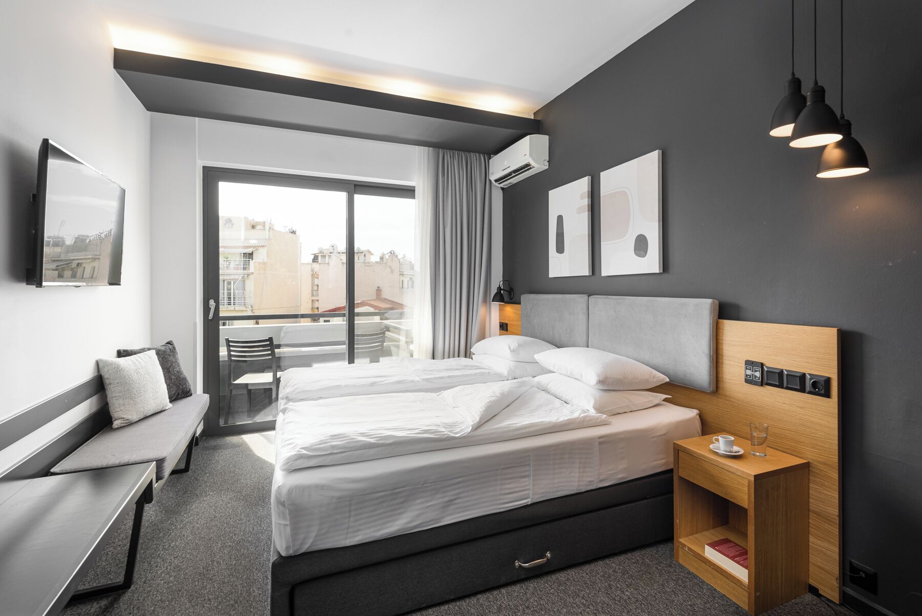 Een moderne hotelkamer met een groot bed, nachtkastje, stoel en uitzicht op de stad door het raam.