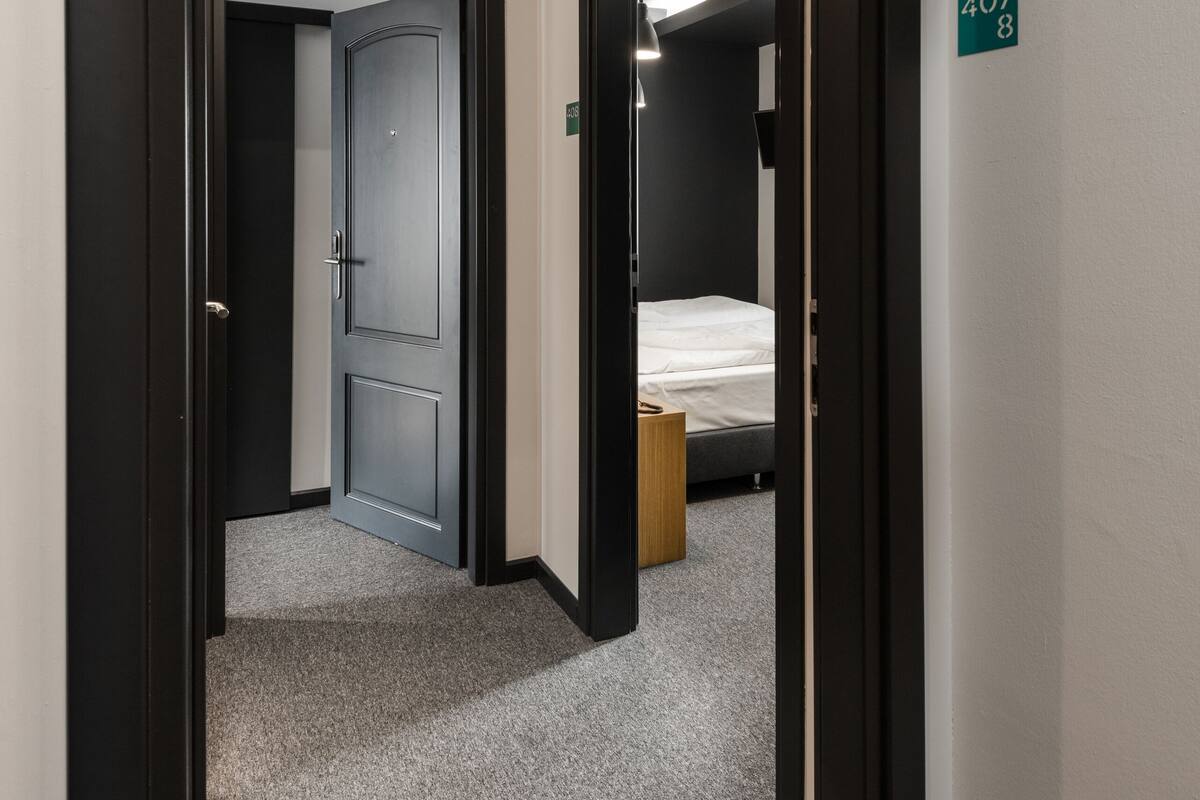 A hotel corridor with a carpeted floor, a door leading to a room with a bed, and a number sign indicating room 4078.