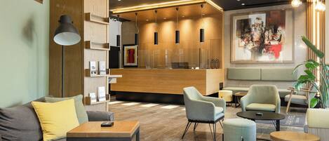 A modern lobby with a grey sofa, wooden flooring, and a reception desk area.