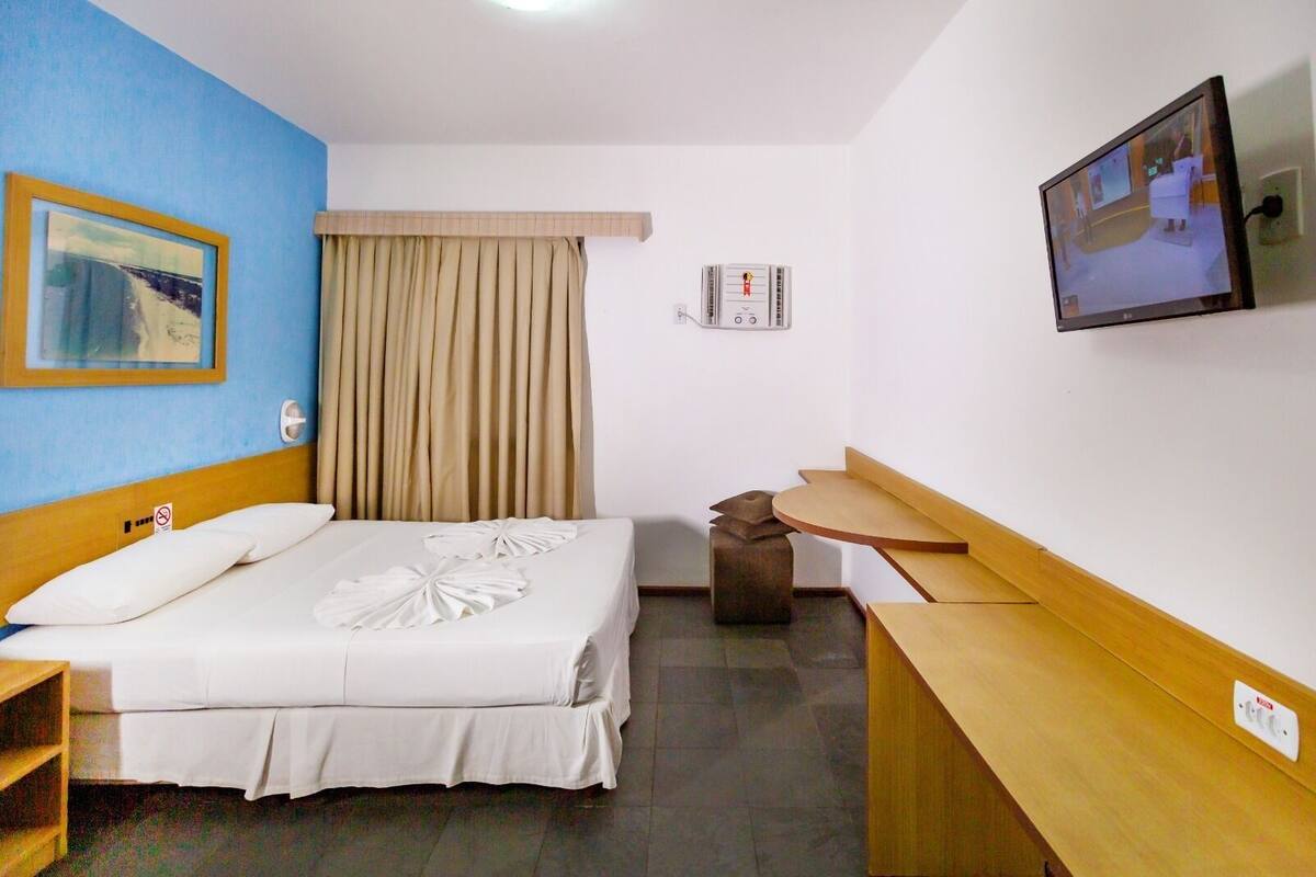 A hotel room with a bed, a television, a desk, and a window with curtains.
