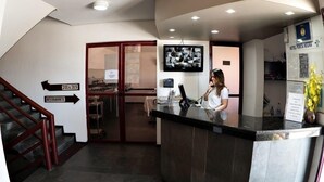 A hotel reception area with a receptionist, a digital screen displaying images, a staircase, and directional signs to the restaurant. - Happy Ponta Negra Express (Natal)