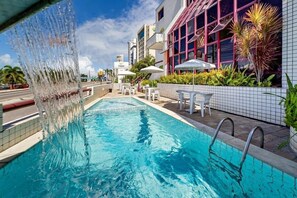 A swimming pool with a water feature, surrounded by outdoor seating and plants.