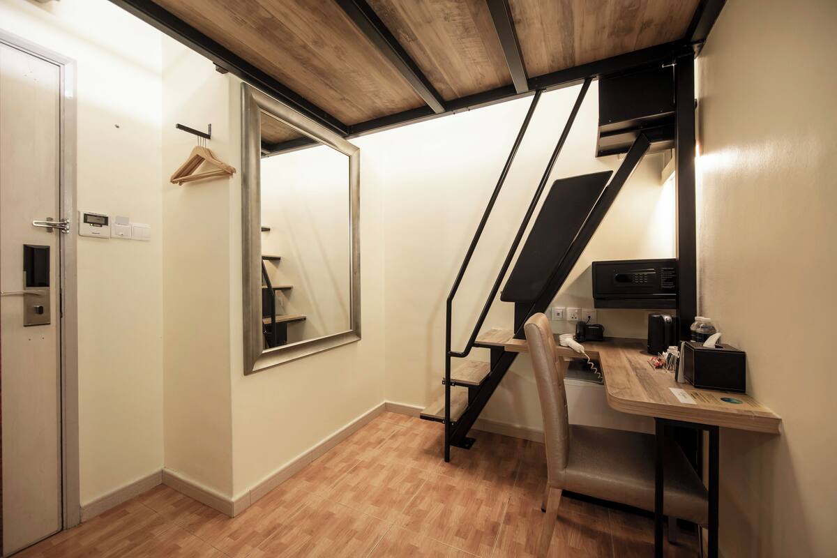 Une chambre moderne avec un plancher en bois, un bureau avec une chaise, un porte-manteau mural, un grand miroir et un escalier avec une rampe noire.