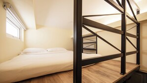 A bunk bed with a wooden platform and metal frame, a single bed with white bedding, and a small window with blinds. - Fragrance Hotel - Balestier (Singapore)