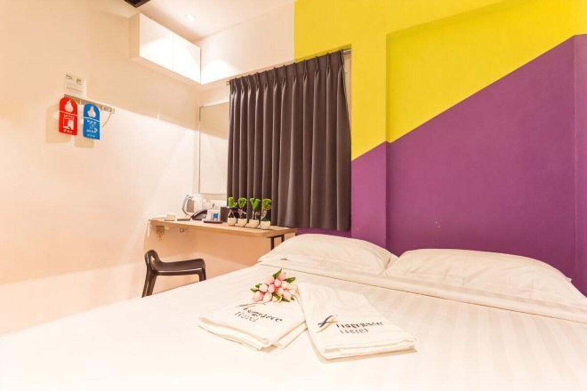 Une chambre d’hôtel avec un lit, un bureau et une chaise, un miroir et une fenêtre avec des rideaux.