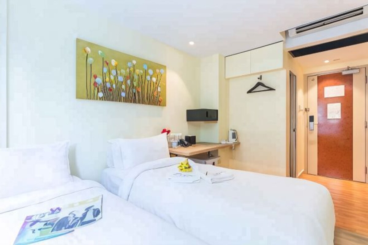 Ein Hotelzimmer mit zwei Betten, einem Bild an der Wand, einem Schreibtisch mit Computer und einer Tür.