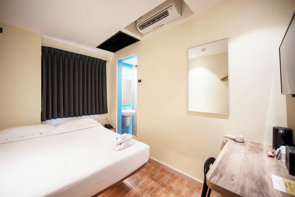 Une chambre d’hôtel avec un lit, un bureau, une chaise, un miroir, un climatiseur et une porte de salle de bain.