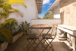 Un pequeño patio exterior con mesa y sillas de madera, rodeado de plantas en macetas y un muro de piedra.