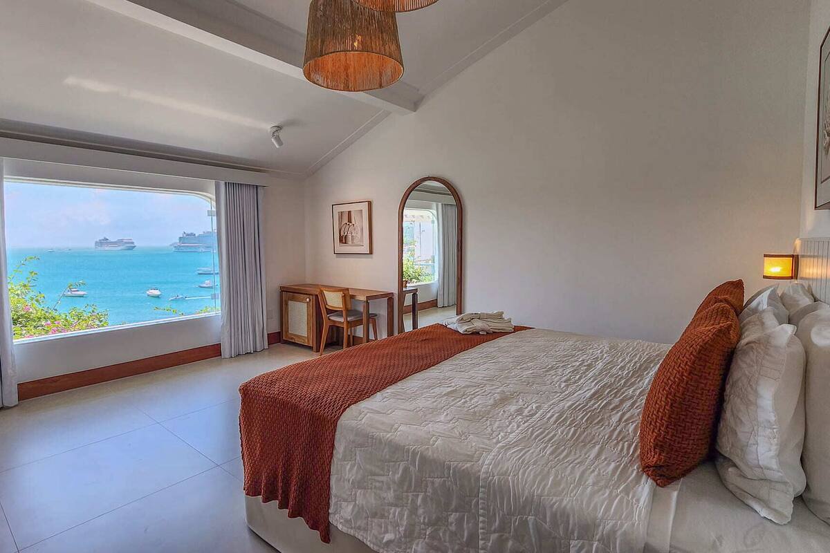 A bedroom with a large bed, a desk, and a view of the sea.