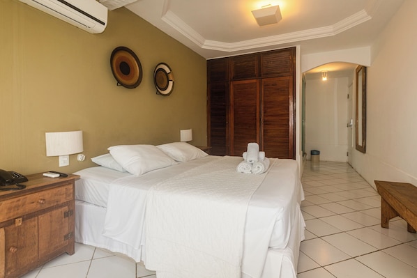 A hotel room with a large bed, a wooden nightstand with a phone, two wall-mounted lamps, and a wooden wardrobe. - Byblos Pousada (Búzios)