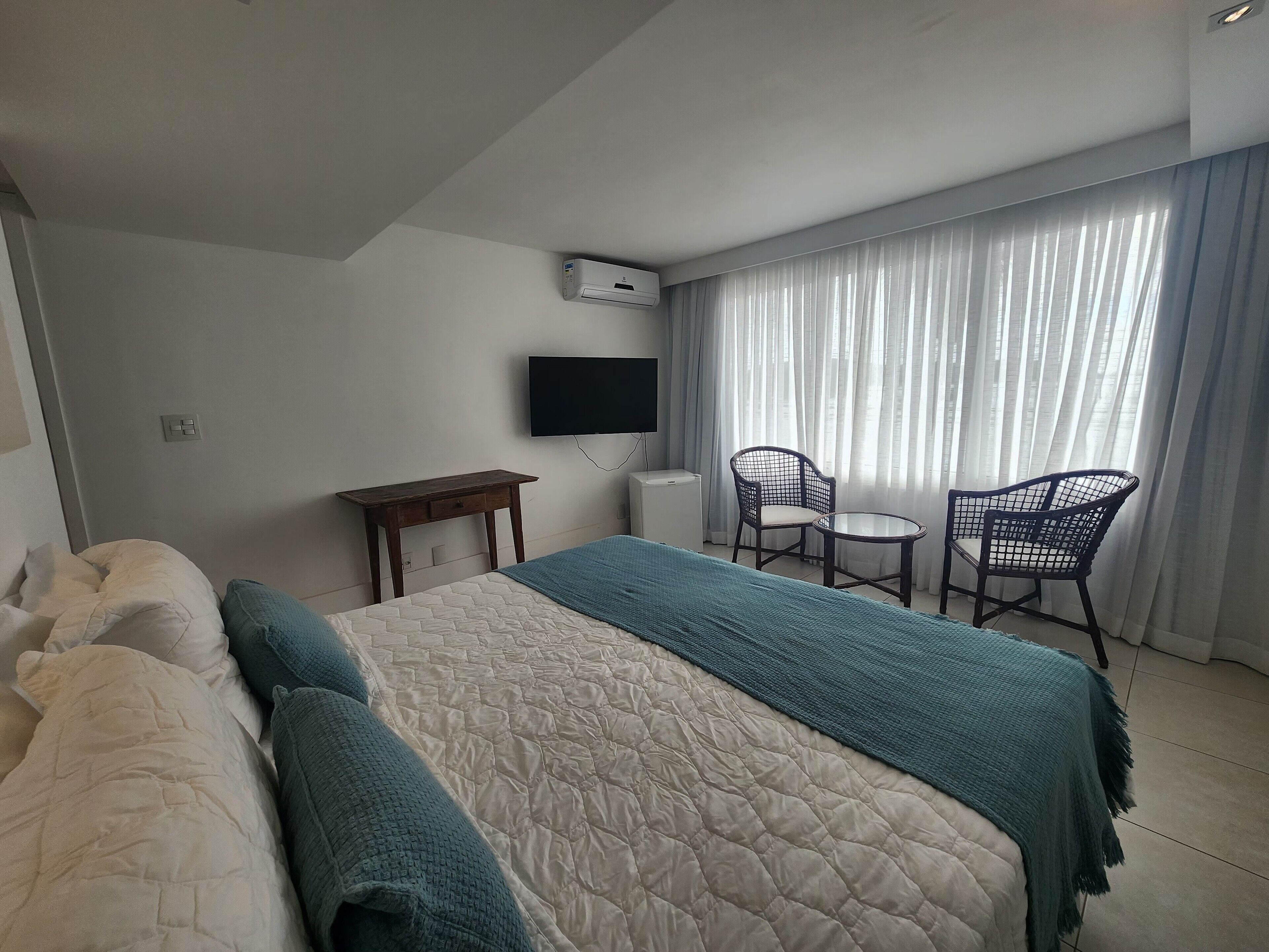 A hotel room with a bed, a desk, two chairs, a TV, and a window with curtains.