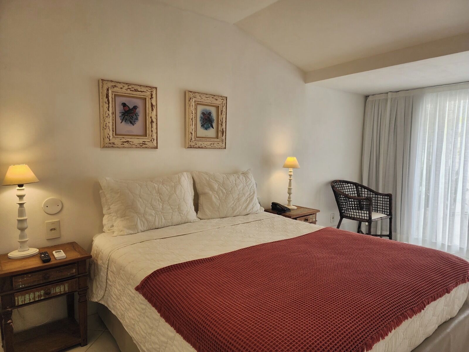 Habitación de hotel con una cama, dos lámparas fijadas a la pared, una silla y dos cuadros enmarcados.