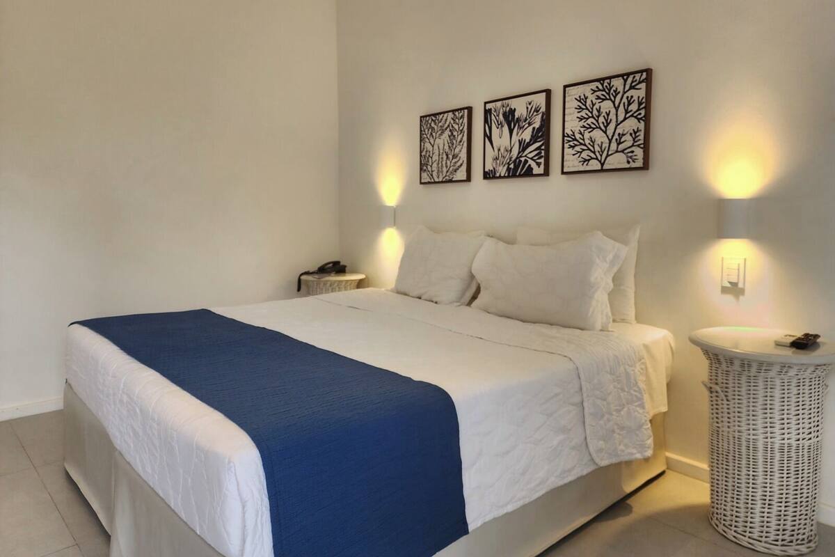 A neatly made bed with a blue and white bedspread, two white pillows, and a headboard. There are three wall-mounted light fixtures on the wall above the bed.