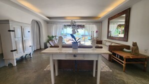 Een ruime kamer met een grote eettafel, een bank en een stoel. Er is uitzicht op het landschap door een raam.