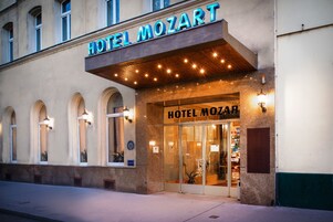 A hotel with a prominent sign reading "HOTEL MOZART" and a classic architectural style with arched windows and a wooden overhang.