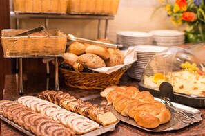 A buffet with various breads, pastries, and a covered dish. - Hotel Mozart (Vienna)