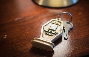 A keychain with "MOZART WIEN" engraved on it, lying on a wooden surface. - Hotel Mozart (Vienna)