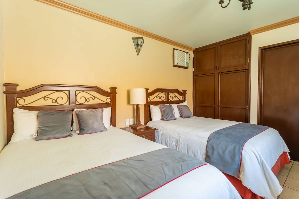 A hotel room with two beds, a nightstand, a lamp, a wardrobe, and a wall-mounted air conditioner.