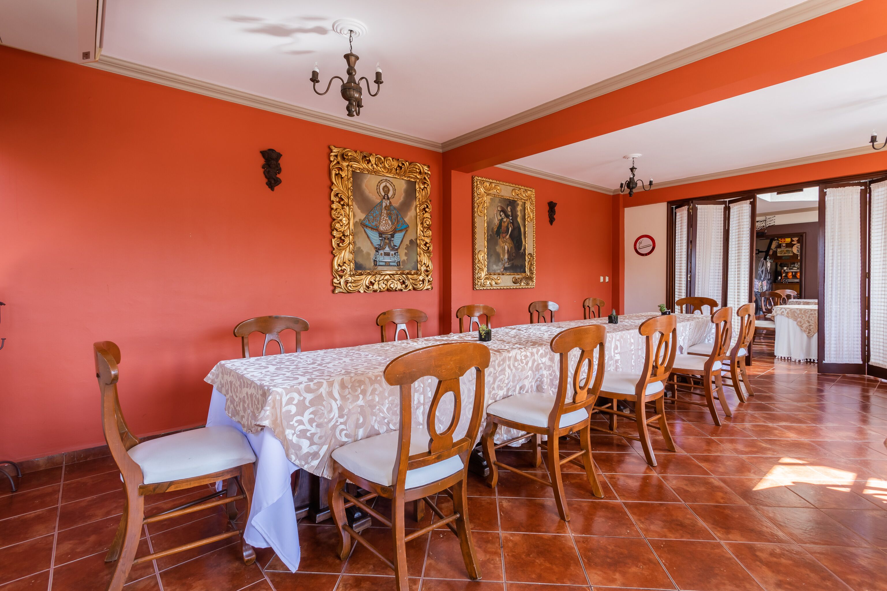A dining area with a long table, chairs, and two framed religious paintings on the walls.