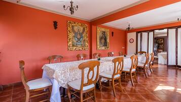 A dining area with a long table, chairs, and two framed religious paintings on the walls.