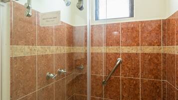 A shower area with a handrail, a sign instructing to slide to open, and a window providing natural light.