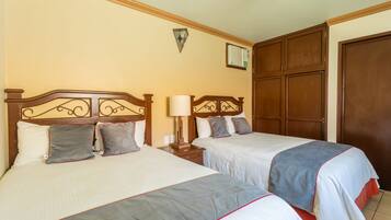 Habitación de hotel con dos camas, cabeceros de madera, una mesita de noche con lámpara, aire acondicionado instalado en la pared y un armario.