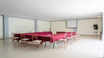A conference room with a long table, chairs, a projector screen, and a speaker on a tripod.