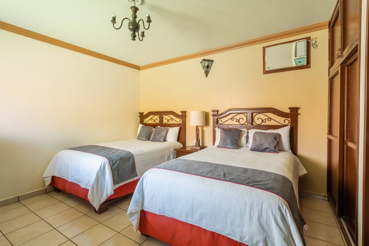 A hotel room with two beds, a chandelier, a wall-mounted air conditioner, and a wooden wardrobe.