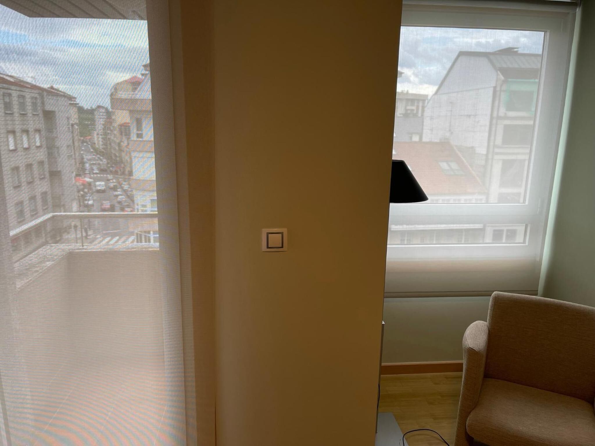 A room with a large window, a chair, and a light switch on the wall.