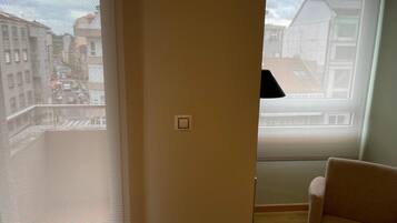 A room with a large window, a chair, and a light switch on the wall.