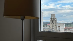 Une vue par la fenêtre sur une tour de pierre historique, avec un bâtiment moderne en premier plan.