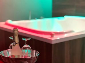 A champagne bottle in a glass bowl on a countertop with a jacuzzi tub in the background.