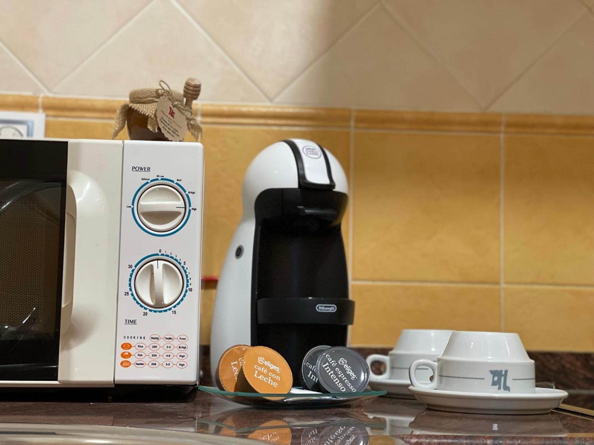 A kitchen with a microwave, coffee maker, and a glass plate with coffee pods.