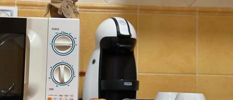 Una cocina equipada con microondas, cafetera y un plato de vidrio con cápsulas de café.