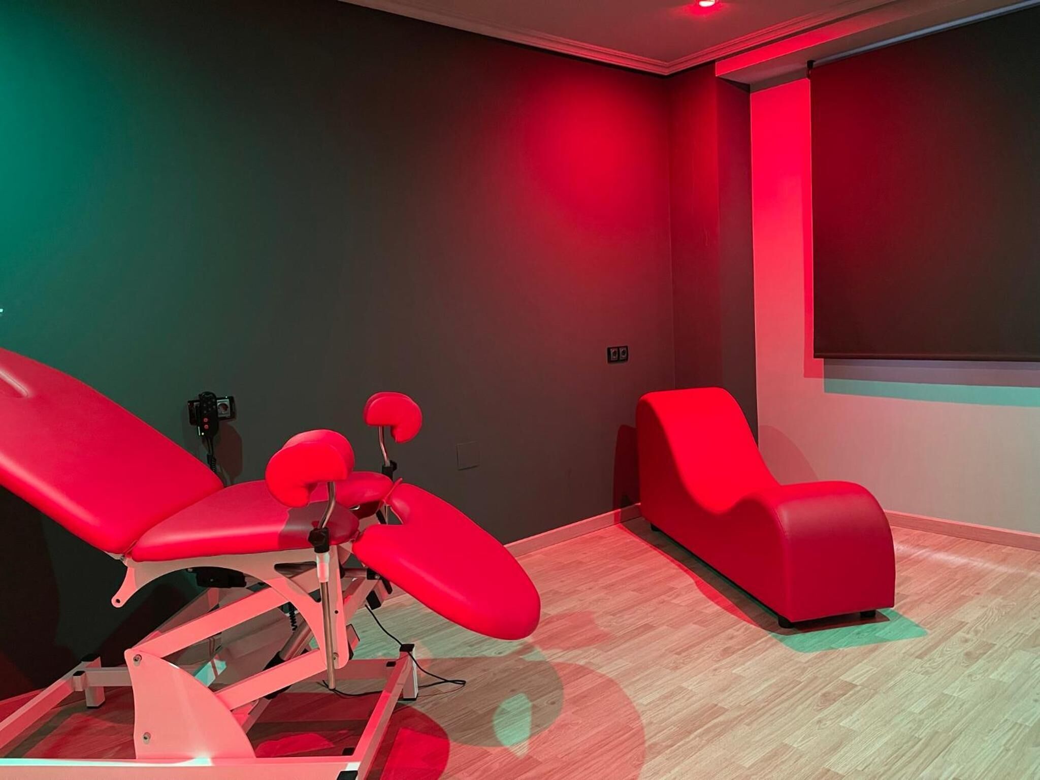 A modern room with a red massage chair, a red recliner, and a large window.